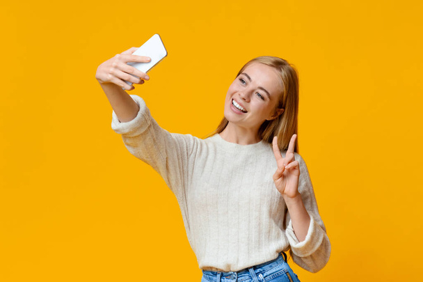 Усміхнена дівчина-підліток бере селфі на смартфон, показуючи мирний жест
 - Фото, зображення