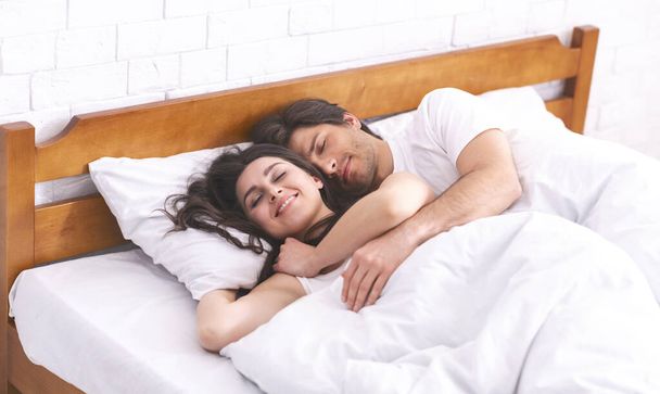 Sevgi dolu erkek ve kadın yatakta uyuyor, birbirlerine sarılıyorlar. - Fotoğraf, Görsel