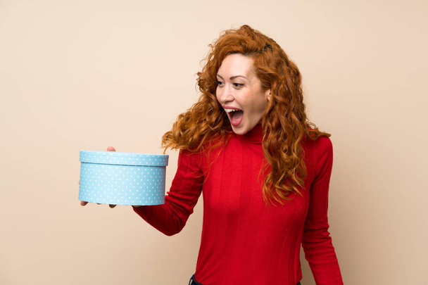 Mujer pelirroja con suéter de cuello alto sosteniendo caja de regalo
 - Foto, Imagen