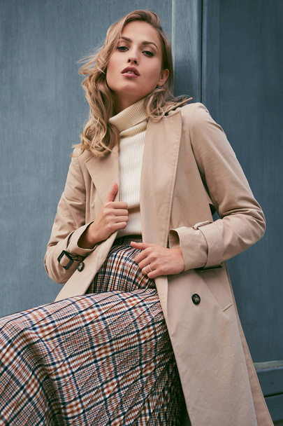 Beautiful casual blond girl in stylish trench coat confidently looking in camera outdoor - Foto, Imagem