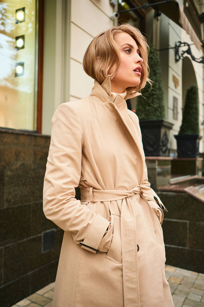 Вид сбоку привлекательной стильной девушки в бежевом пальто на городской улице
 - Фото, изображение