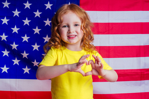 redhead ginger charming female kid celebration independence holding american flag on a pink background in the studio.English language learning concept and freedom dream making a heart figure fingers - Foto, immagini