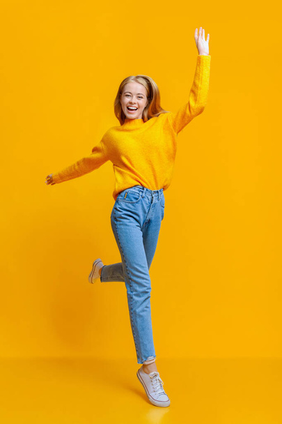 positive Teenager-Mädchen zu Fuß auf Luft über orange Studio Hintergrund - Foto, Bild