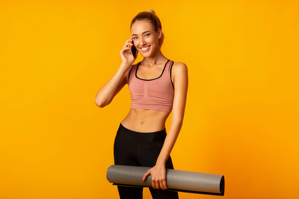 Hölgy beszél telefonon Holding Fitness Mat álló, sárga háttér - Fotó, kép