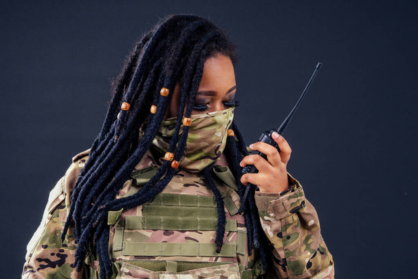 Woman in a military camouflage with a radio afro american army latin soldier in camouflage clothes hair dreadlocks evening makeup on a black background in the studio. - Foto, Imagem