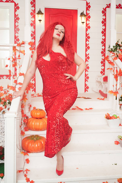 Νεαρή στιλάτη παχουλή γυναίκα με κόκκινο maxi φόρεμα στη βεράντα του Λευκού Οίκου της. Φθινοπωρινή μόδα, κομψή εμφάνιση. Συν μέγεθος μοντέλο. - Φωτογραφία, εικόνα