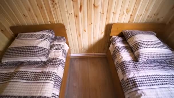 Het interieur van een kleine schone hotelkamer met twee bedden, goedkope accommodatie concept. Kunst. Een kamer met houten muren en vloer en twee smalle bedden. - Video