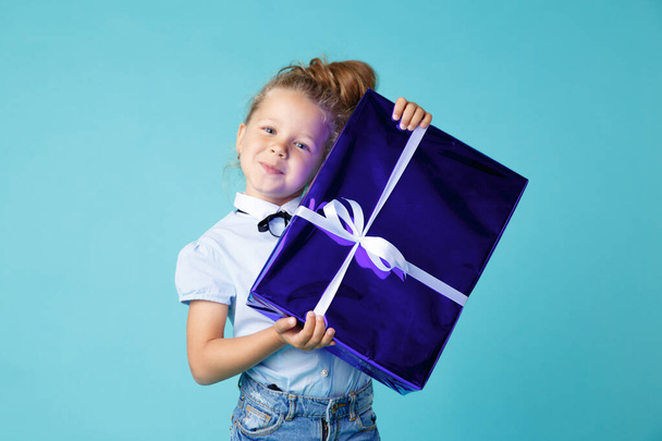 Holčička s velkým modrým dárkem v krabici s bílou stuhou. Novoroční dárkový poukaz. - Fotografie, Obrázek