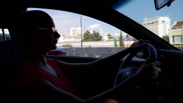 Young beautiful bald woman in sunglasses sitting at the wheel of a car on a summer day. car trip - Fotó, kép