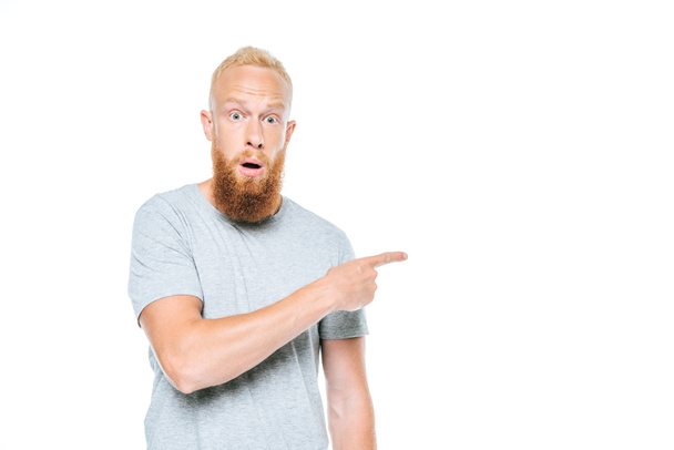 handsome bearded shocked man in grey t-shirt pointing isolated on white - Фото, зображення