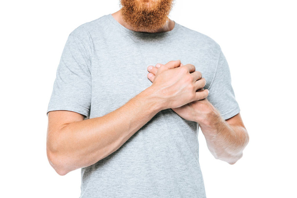 levágott kilátás szakállas férfi szürke póló fogja a kezét a szív, elszigetelt fehér - Fotó, kép