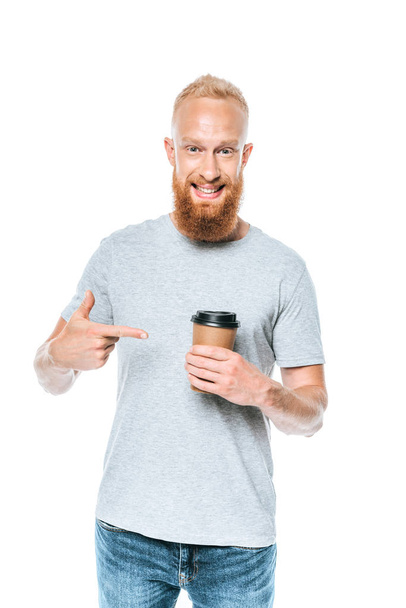 smiling bearded man in t-shirt pointing at coffee to go, isolated on white - Photo, Image