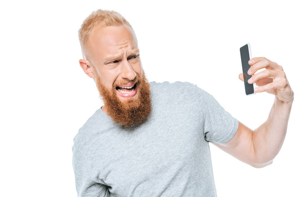 agressieve man schreeuwen en kijken naar smartphone met leeg scherm, geïsoleerd op wit - Foto, afbeelding