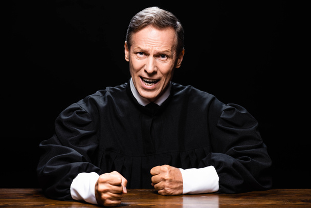 судья в судейском халате сидит за столом и смотрит в камеру и кричит изолированные на черный
 - Фото, изображение