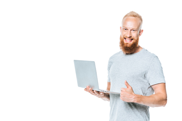 cheerful bearded man using laptop and showing thumb up, isolated on white - Valokuva, kuva