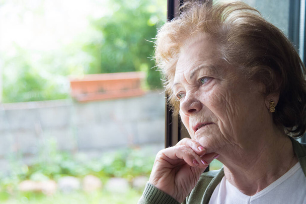 Yaşlı kadın pencereden dışarı bakıyor, son sınıflar. - Fotoğraf, Görsel
