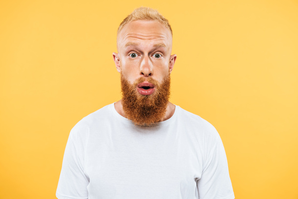 portrait of surprised handsome bearded man looking at camera, isolated on yellow - Foto, immagini
