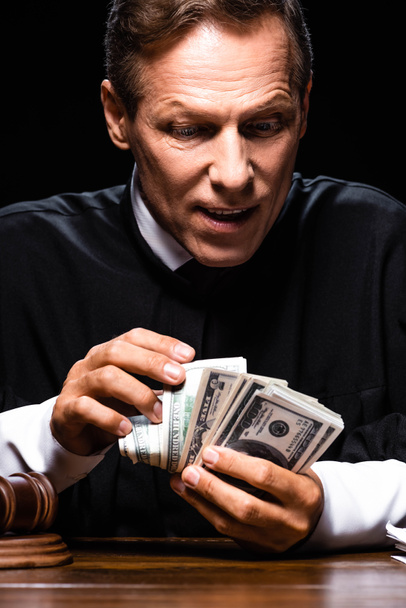 juge en robe judiciaire assis à table et comptant billets en dollars isolés sur noir
 - Photo, image