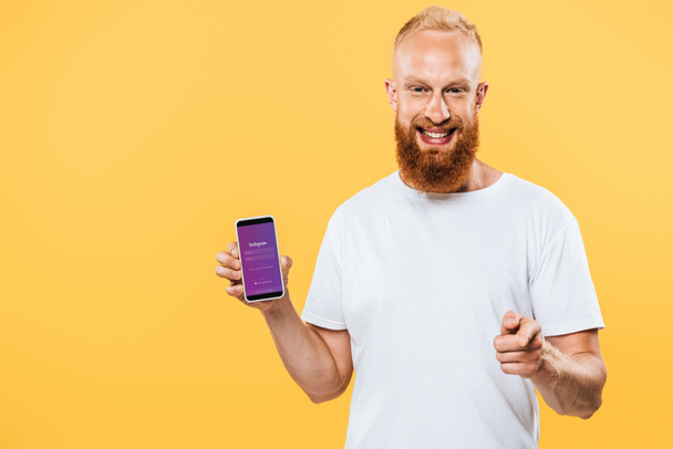 Kijev, Ukrajna - augusztus 27, 2019: mosolygós szakállas férfi bemutató okostelefon Instagram app és rámutatva rád, elszigetelt sárga - Fotó, kép