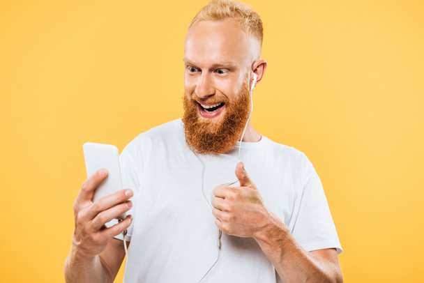 cheerful bearded man with earphones taking selfie on smartphone and showing ok sign, isolated on yellow - Foto, immagini