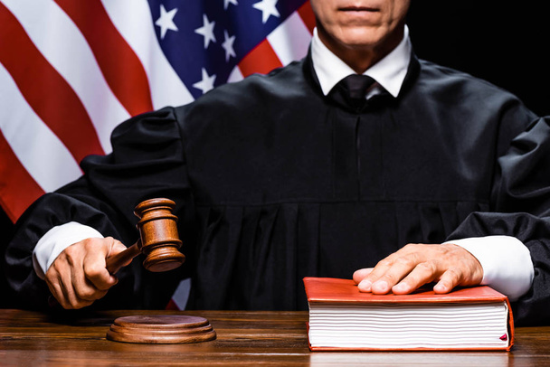 обрезанный взгляд судьи в судейском халате, ударяющего молотком и кладущего руку на книгу
  - Фото, изображение