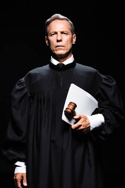 δικαστής με δικαστικό χιτώνα κρατώντας σφυρί και έγγραφα που απομονώνονται σε μαύρο  - Φωτογραφία, εικόνα