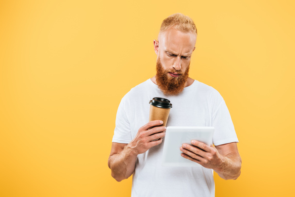 Kahve getiren düşünceli sakallı adam dijital tablet kullanıyor, sarı tablet üzerinde izole edilmiş. - Fotoğraf, Görsel