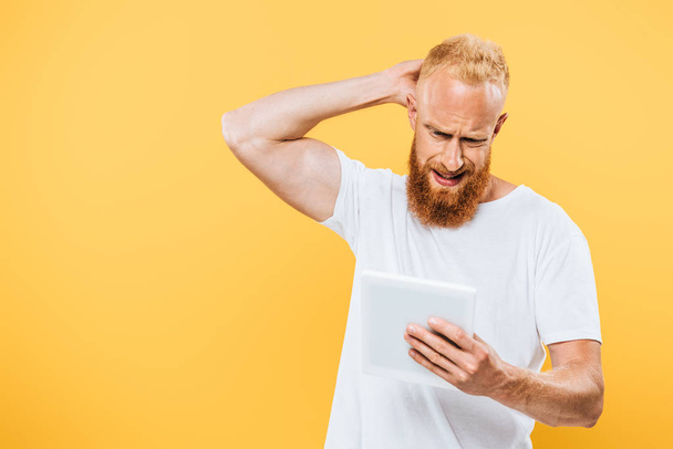 worried bearded man using digital tablet, isolated on yellow - Photo, image