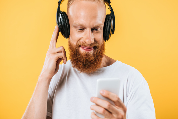 homem de barba sorridente ouvindo música com fones de ouvido e smartphone, isolado em amarelo
 - Foto, Imagem