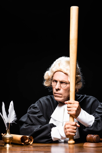 судья в судейском халате и парике сидит за столом и держит летучую мышь изолированной на черном
 - Фото, изображение