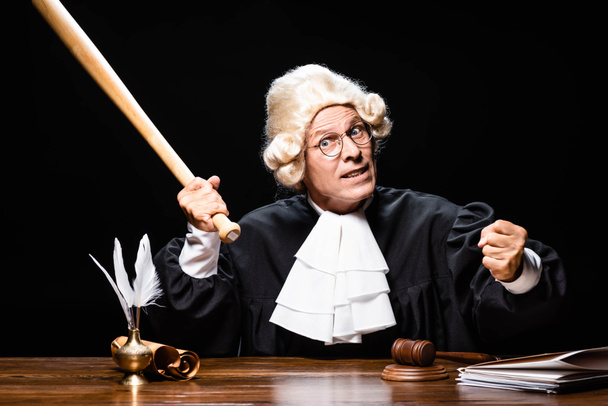 juez enojado en bata judicial y peluca sentado a la mesa y sosteniendo murciélago aislado en negro
 - Foto, Imagen
