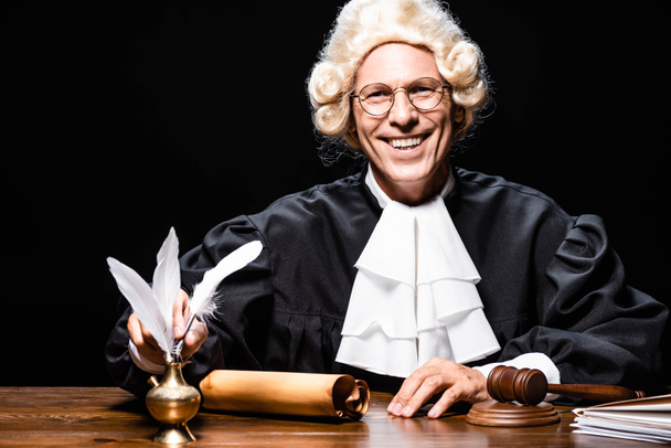 giudice sorridente in veste giudiziaria e parrucca prendendo piuma isolata su nero
 - Foto, immagini