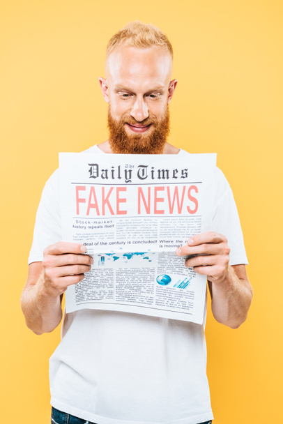 homem barbudo sorridente lendo jornal com notícias falsas, isolado no amarelo
 - Foto, Imagem