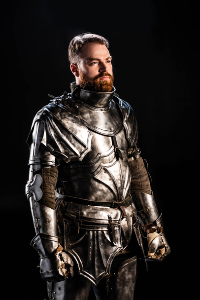 handsome knight in armor looking away isolated on black - Foto, imagen