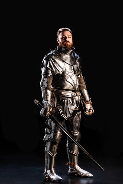 schöner Ritter in Rüstung mit Schwert isoliert auf schwarz  - Foto, Bild
