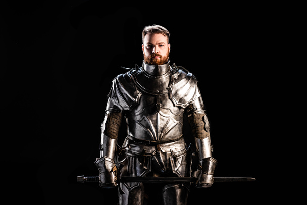 handsome knight in armor holding sword isolated on black - Zdjęcie, obraz