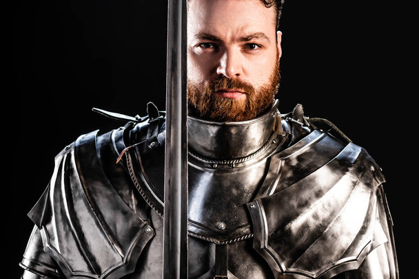 handsome knight in armor holding sword isolated on black - Photo, Image