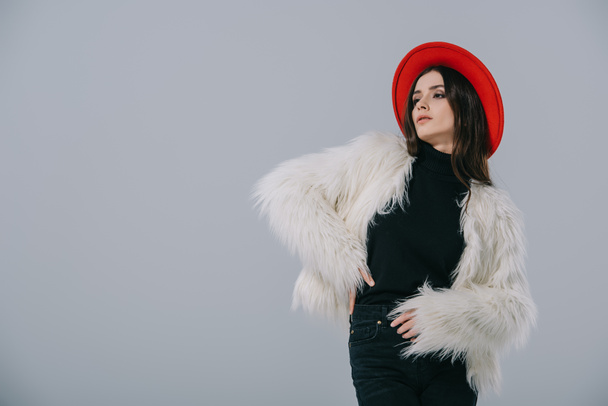 attractive elegant woman posing in white fur coat and red hat, isolated on grey - Foto, afbeelding