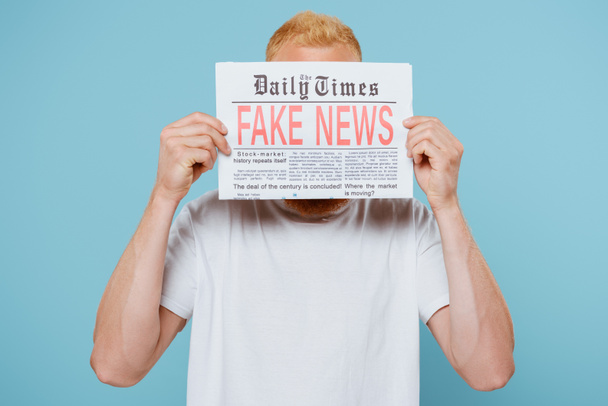 man holding newspaper with fake news in front of face, isolated on blue - Fotografie, Obrázek