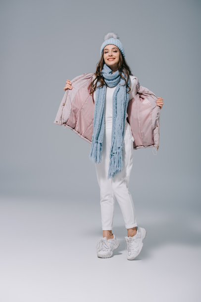 happy girl posing in warm coat, knitted hat and scarf on grey - Photo, Image