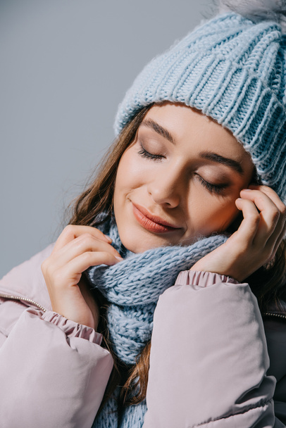beautiful woman posing with closed eyes in knitted hat and scarf, isolated on grey - Foto, afbeelding