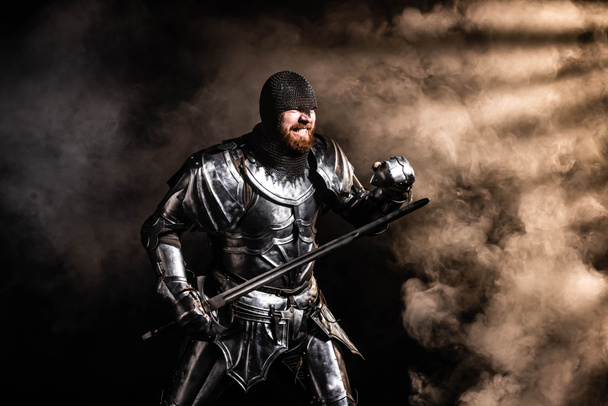 handsome knight in armor holding sword and fighting on black background - Valokuva, kuva