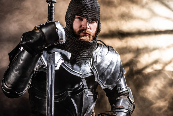 handsome knight in armor holding sword on black background - Fotoğraf, Görsel