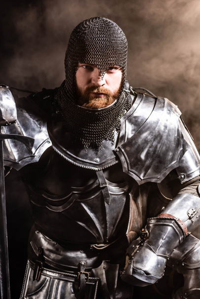 Siyah arka planda kılıç tutan zırhlı yakışıklı bir şövalye. - Fotoğraf, Görsel