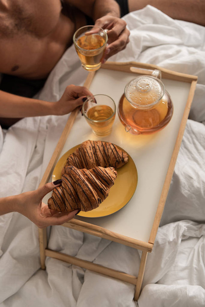 vista recortada de la pareja tomando té y croissants para el desayuno en la cama por la mañana
   - Foto, imagen
