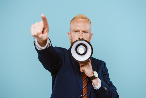 angry bearded businessman pointing and shouting into megaphone, isolated on blue - Foto, immagini