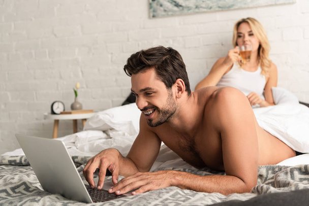 jóképű férfi használ laptop az ágyban barátnő ivás tea mögött - Fotó, kép