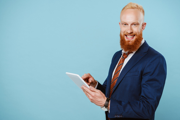 homem de negócios barbudo feliz em terno usando tablet digital, isolado em azul
 - Foto, Imagem