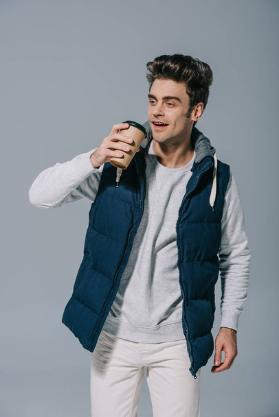 feliz hombre guapo en chaleco caliente beber café para llevar, aislado en gris
 - Foto, imagen