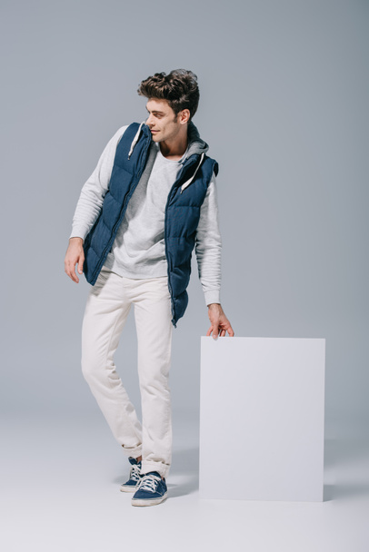 handsome stylish man in waistcoat posing with empty board on grey - Fotoğraf, Görsel